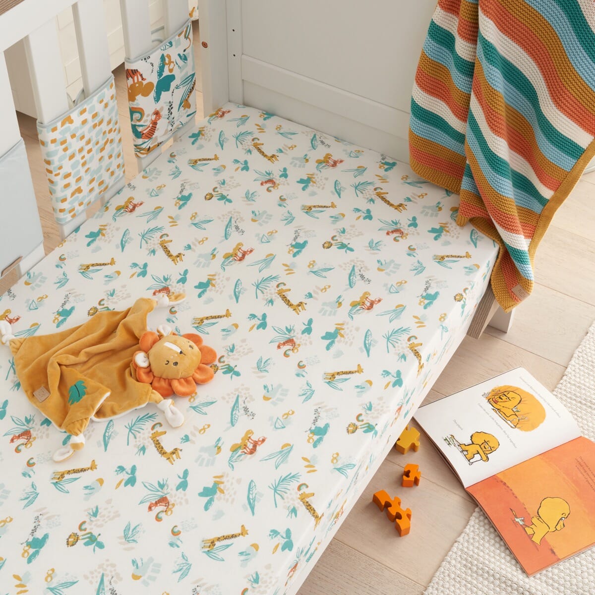 Lifestyle view of cot fitted sheet in Run Wild design, jungle-inspired cotton fabric with colourful animal prints for a snug nursery