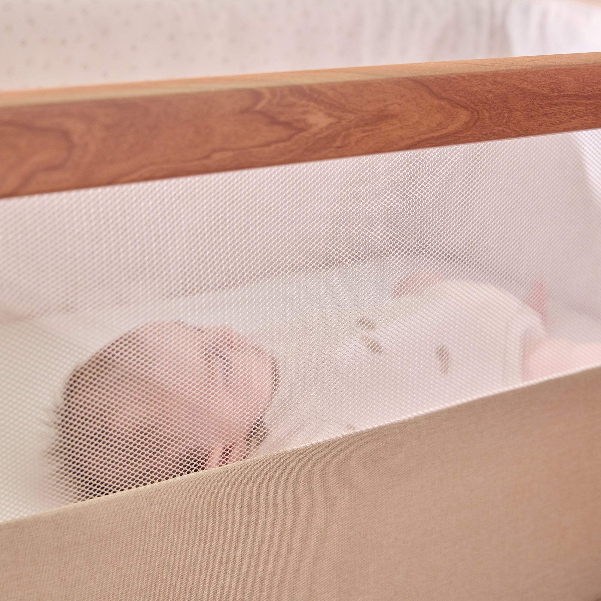 Baby sleeping peacefully inside the CoZee bedside crib in Scandinavian Ecru, viewed through the breathable mesh side for visibility and airflow