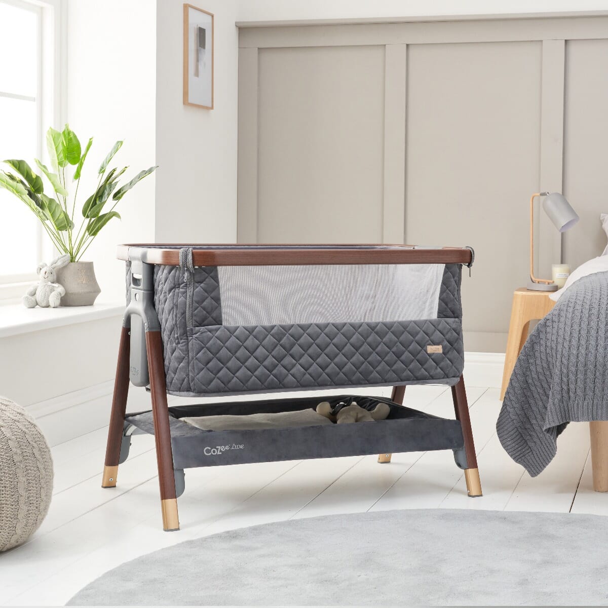 Styled nursery scene featuring the CoZee Luxe bedside crib in walnut and slate with soft quilted lining and breathable mesh siding