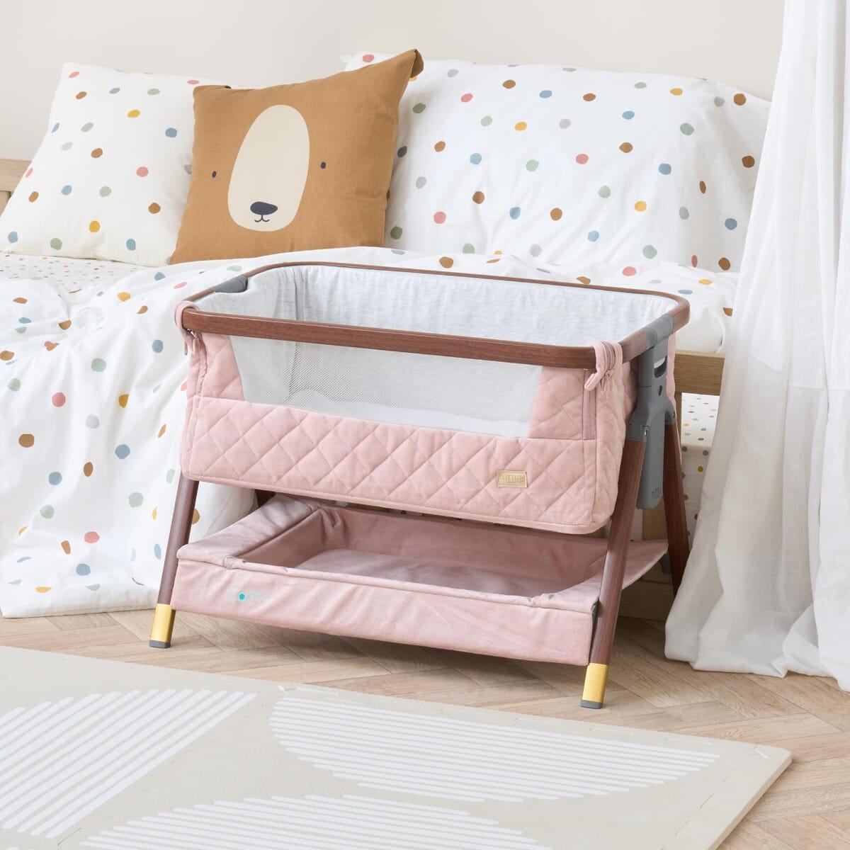 Styled nursery scene featuring the CoZee Luxe Mini Me crib in walnut and blush, highlighting quilted detailing and mesh side panel