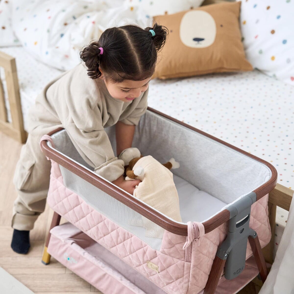 Close-up of toddler smiling while playing with plush toy in the CoZee Luxe Mini Me crib in walnut and blush, showing soft grey lining and mesh sides
