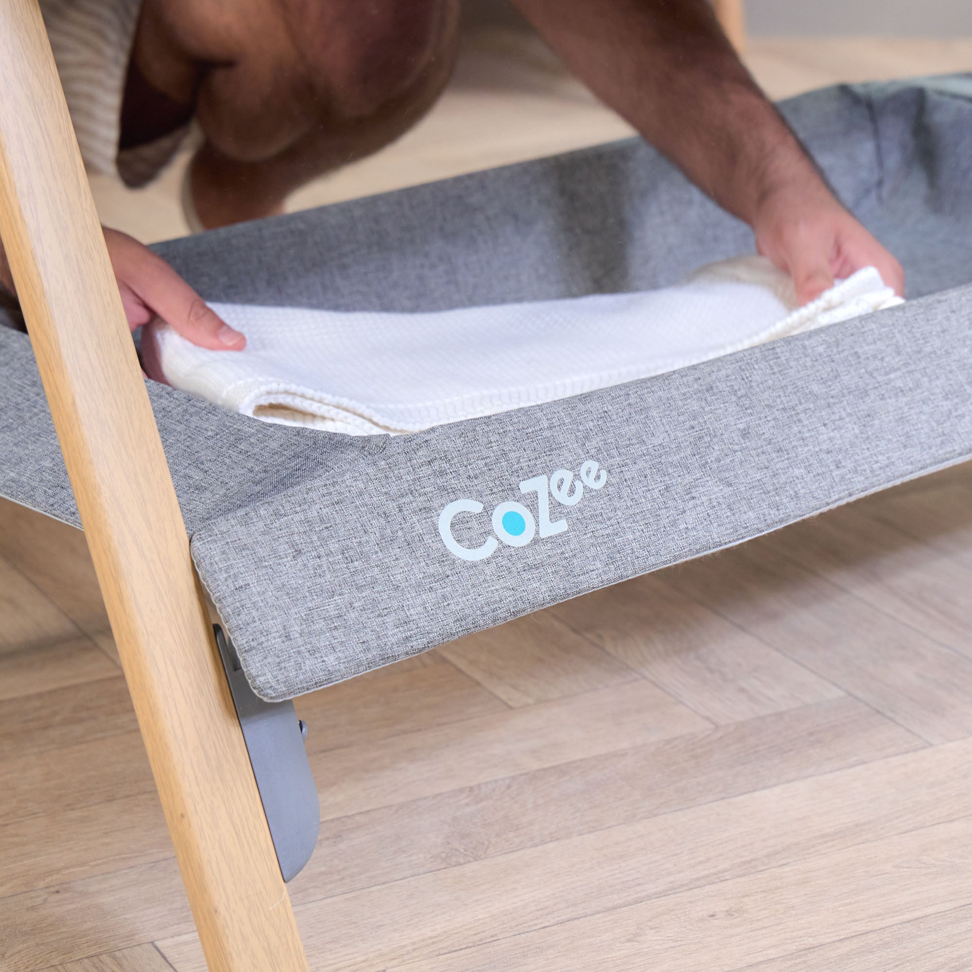 Close-up of the CoZee bedside crib storage shelf in oak and charcoal with white blanket inside, ideal for keeping essentials close to hand