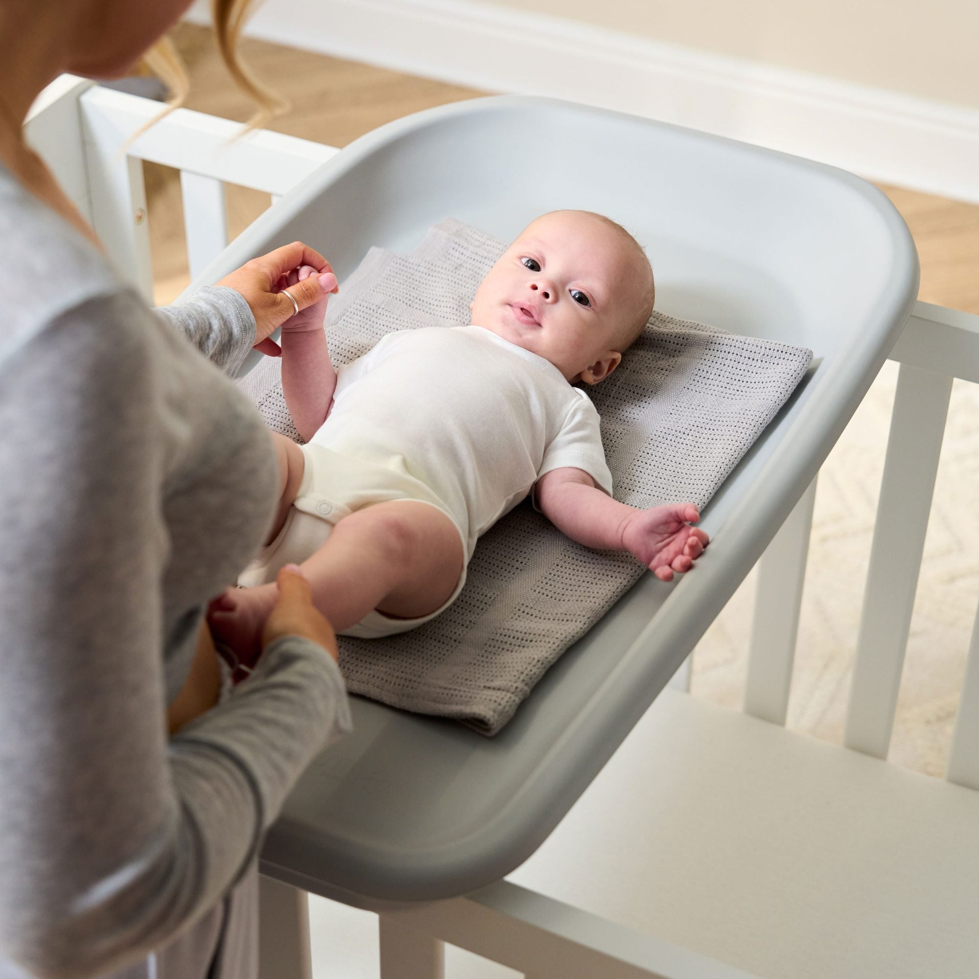Overhead view of baby lying safely on the Cushi baby changing mat in cloud grey, supported with cot-top design and raised sides