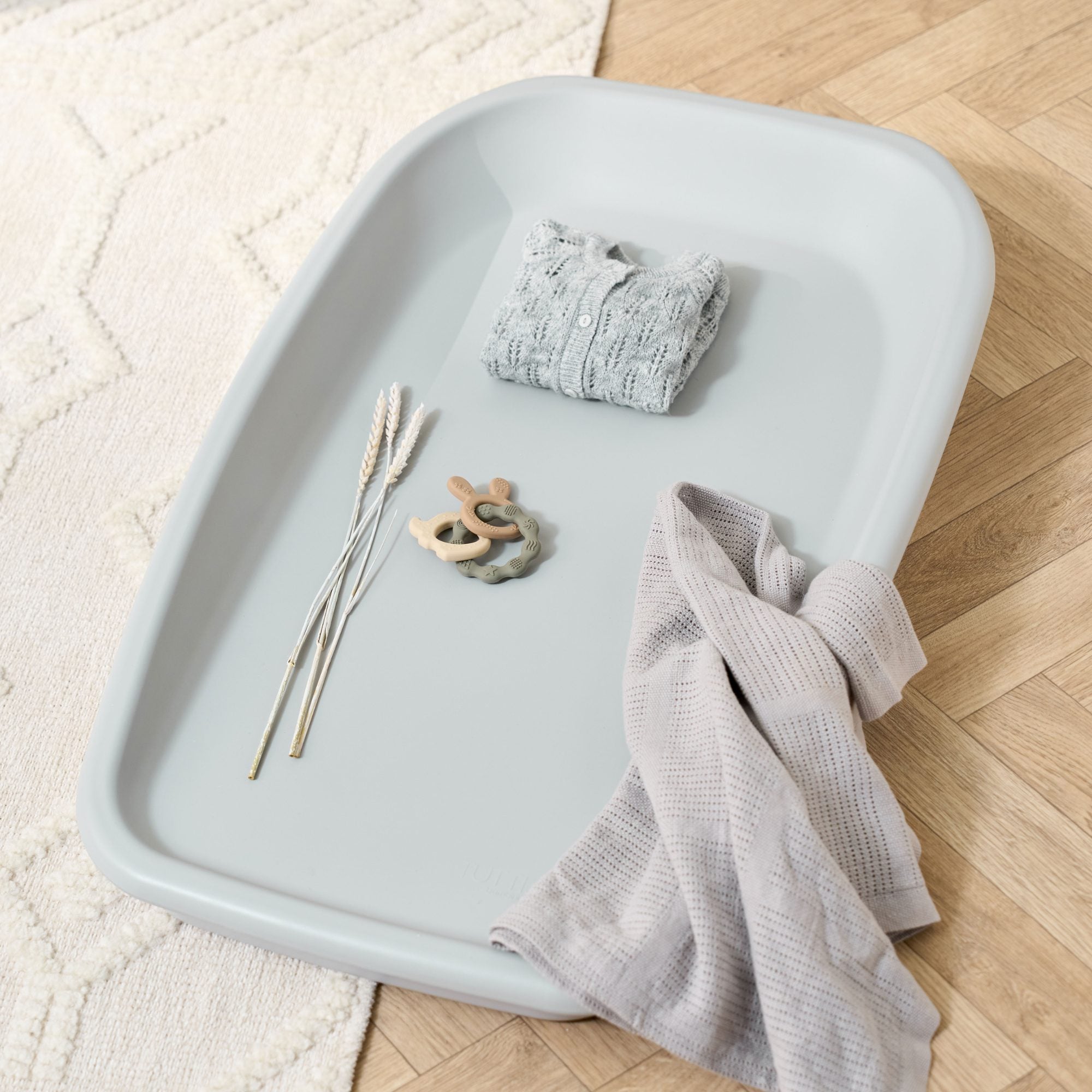 Lifestyle view of the Cushi baby changing mat in cloud grey, styled with blanket and toy, showing practical cot-top changing design