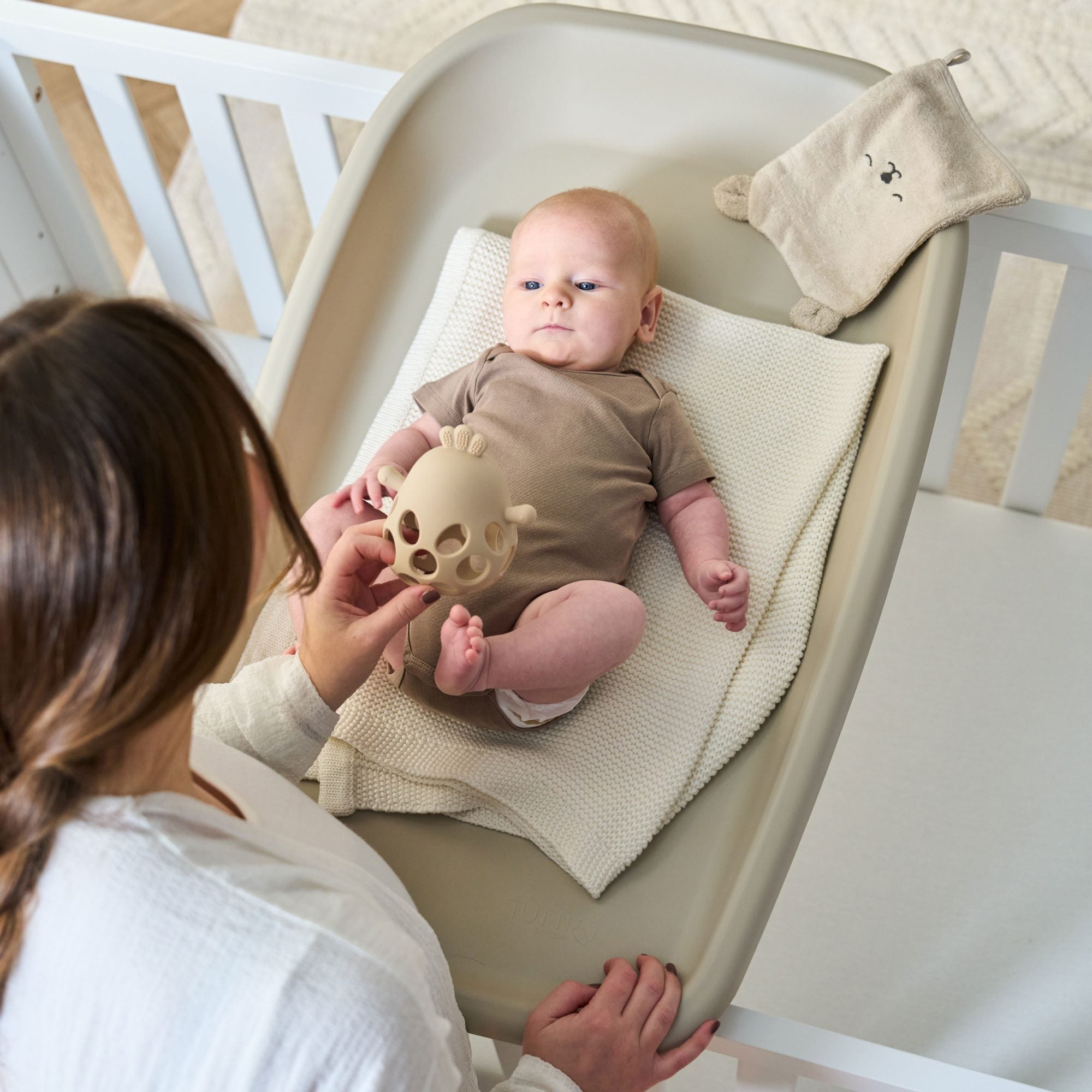 Overhead view of baby on the Cushi changing mat in mushroom with parent close by, capturing bonding during nappy changes
