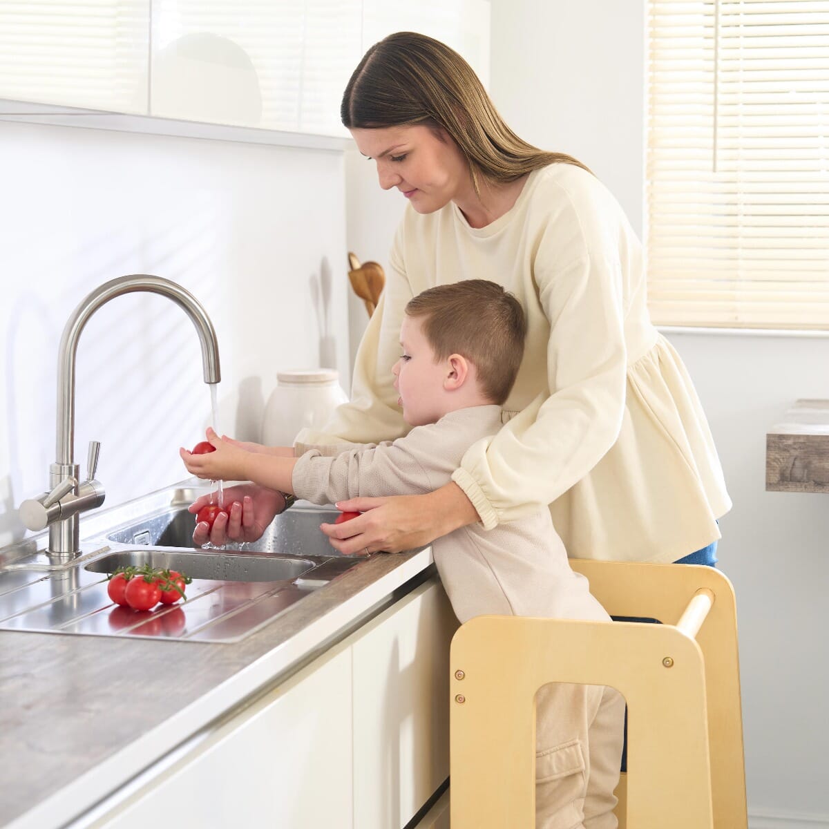 Toddler helps with food preparation at the counter using the Helping Hands Montessori learning tower in natural wood finish, fostering independence