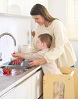 Toddler helps with food preparation at the counter using the Helping Hands Montessori learning tower in natural wood finish, fostering independence
