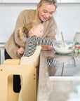 Close-up of mum and toddler at the kitchen counter with the Helping Hands Montessori learning tower in natural finish, encouraging hands-on learning.