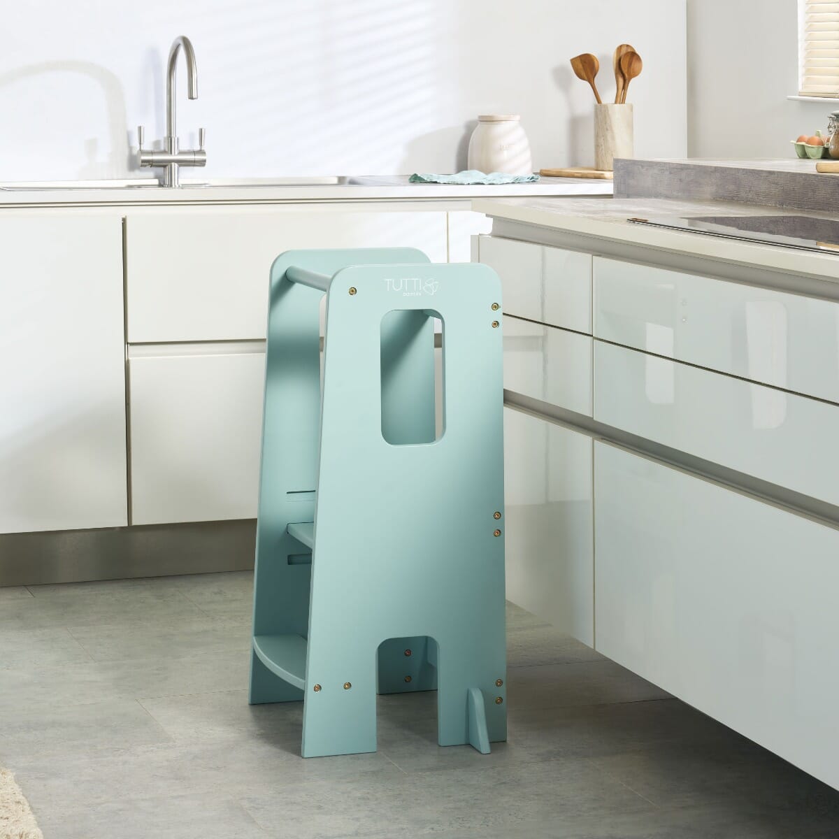 Lifestyle kitchen view of the Helping Hands Montessori toddler learning tower in ocean stone, placed by counter for safe child participation