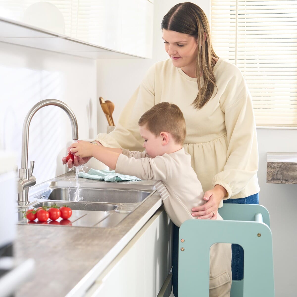 Toddler washing tomatoes at the sink with mum using the Helping Hands Montessori learning tower in ocean stone for safe counter access