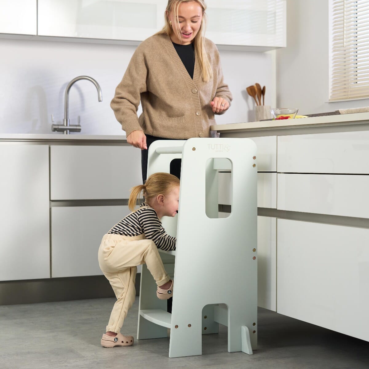 Toddler climbing up the Helping Hands Montessori Learning Tower in sea mist, demonstrating stable steps and safety handles for support