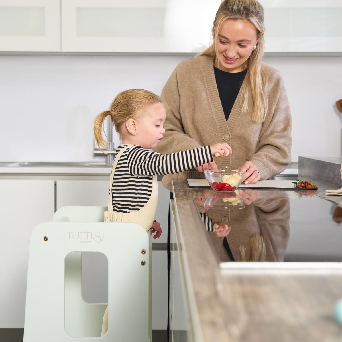 Toddler preparing food with mum using the Helping Hands Montessori Learning Tower in sea mist, fostering independence and family interaction