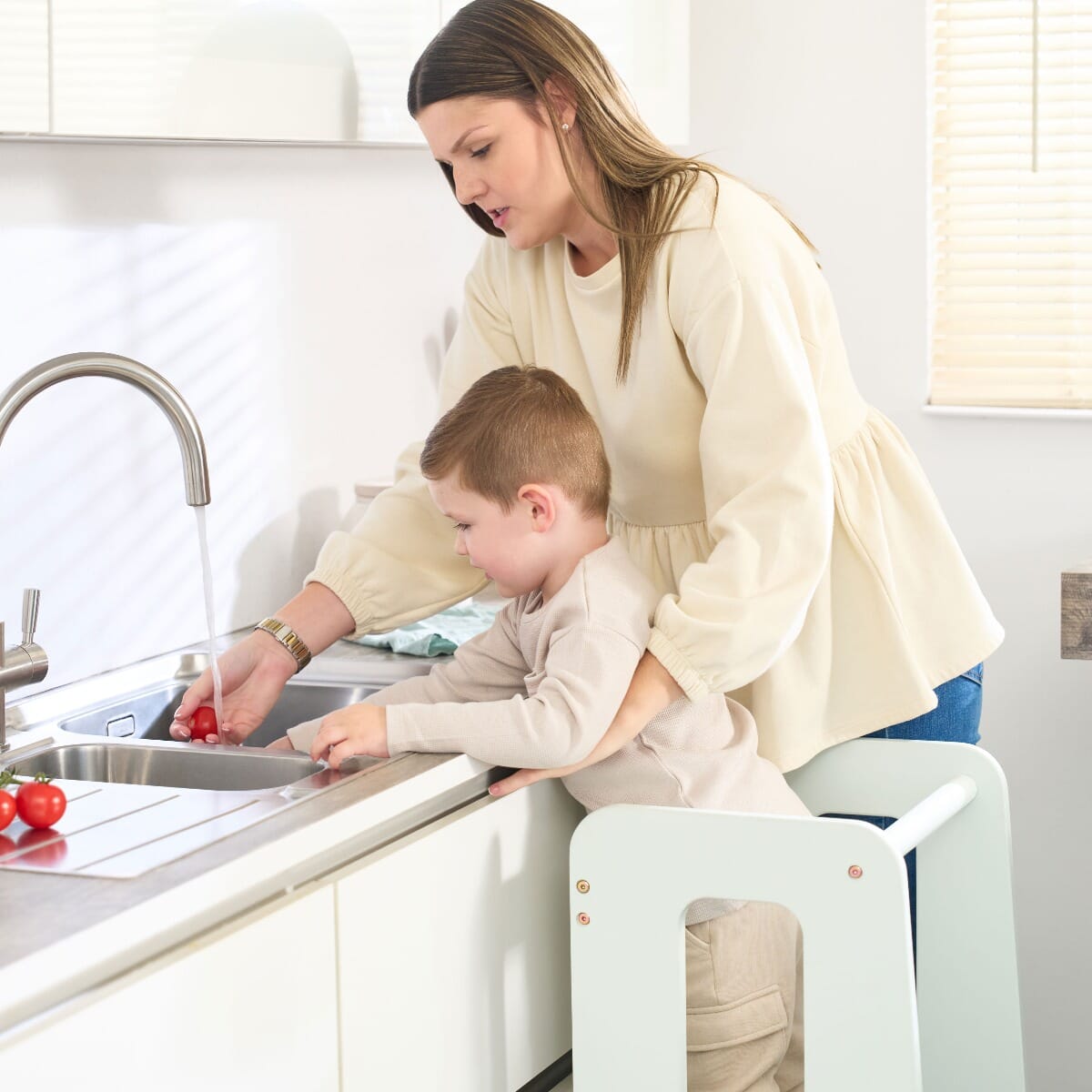 Toddler standing in the Helping Hands Montessori Learning Tower in sea mist at the sink with mum, safely engaged in washing tomatoes