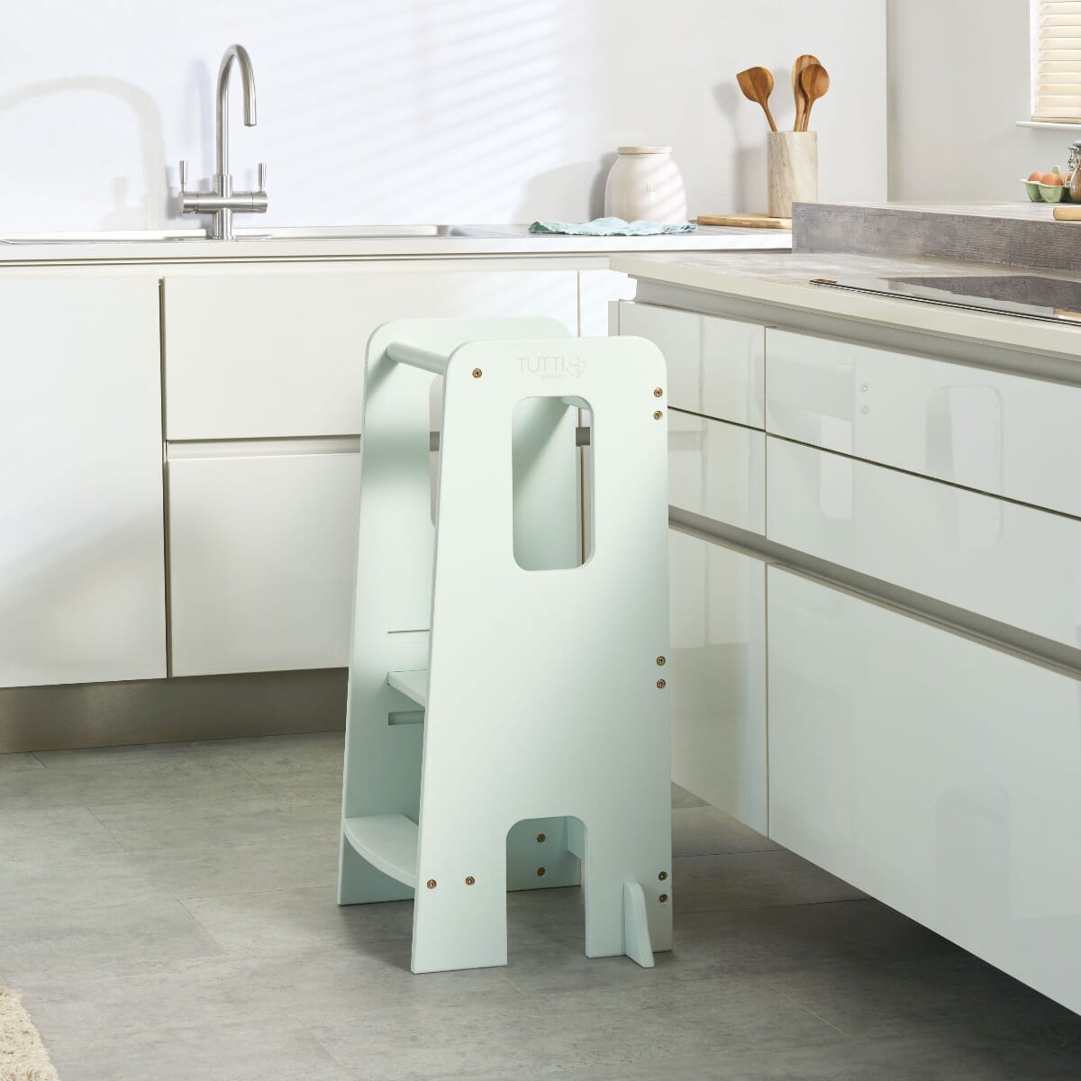 Helping Hands Montessori Toddler Learning Tower in sea mist placed at a kitchen counter, designed to encourage safe toddler participation