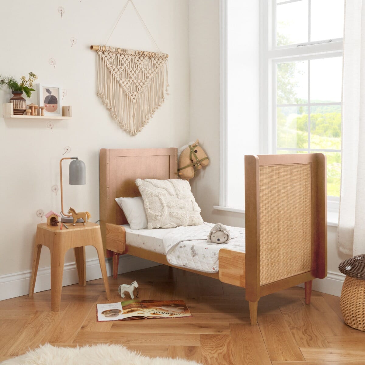 Japandi cot bed in light oak converted to toddler bed mode, styled in a modern nursery with natural décor and soft textiles, showcasing the cane panel detailing on the footboard.