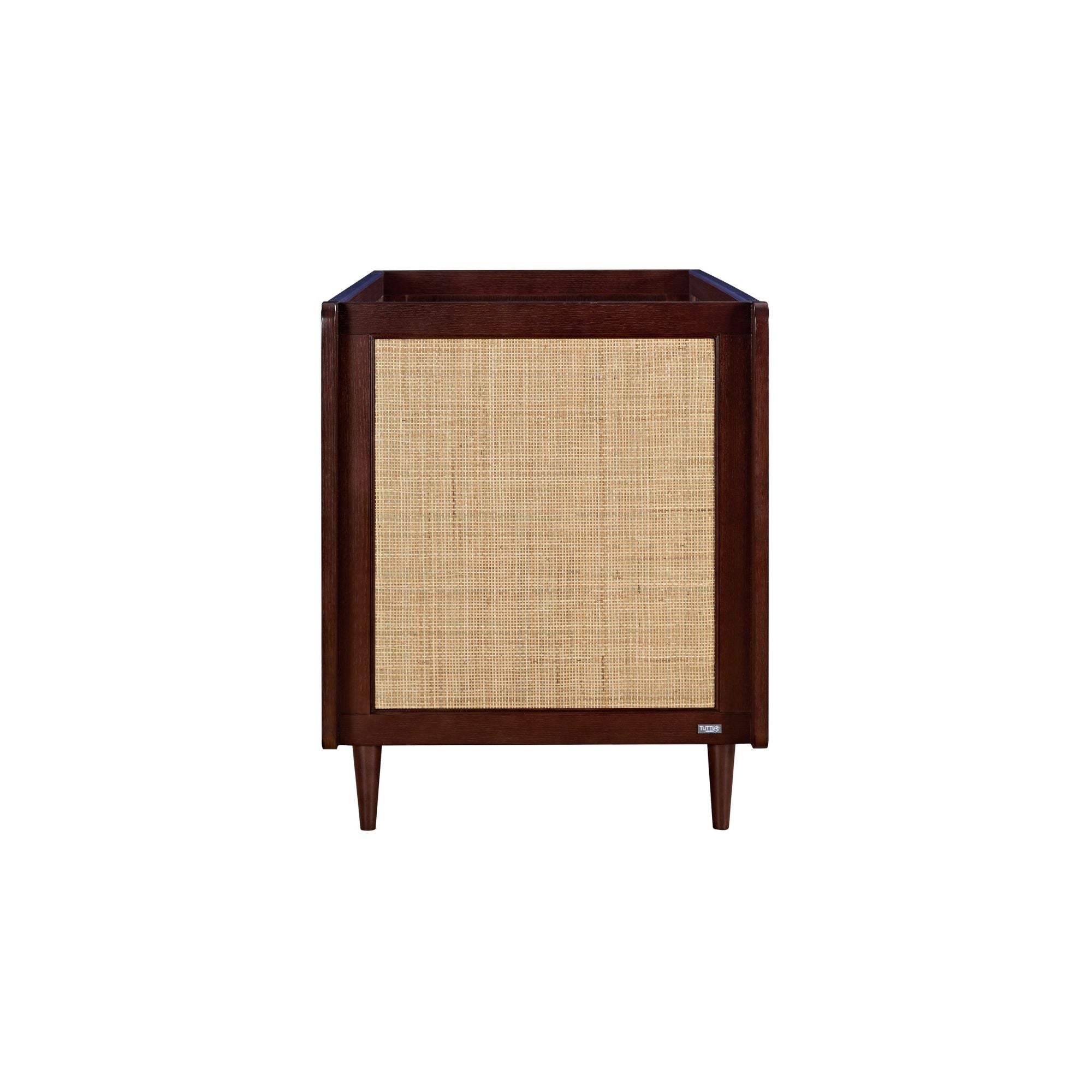 Japandi cot bed in warm walnut shown from the side, highlighting the natural rattan panel and smooth finish on tapered legs.