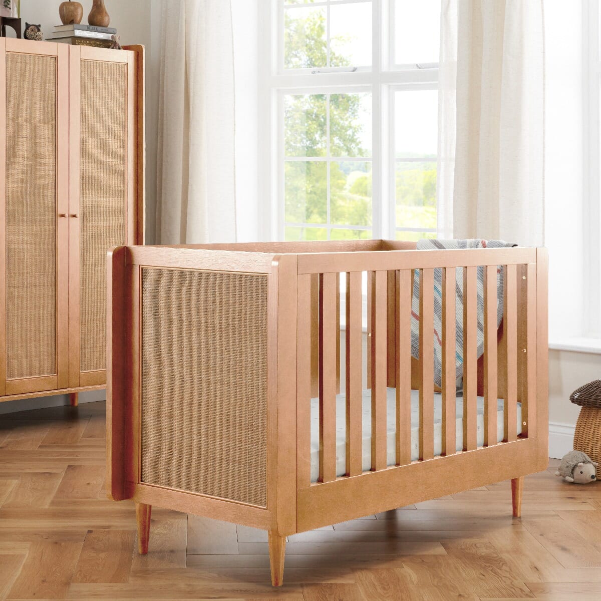 Japandi mini cot bed in light oak with cane side panels, displayed in a nursery room with soft natural lighting and boho decor, highlighting its transitional design.