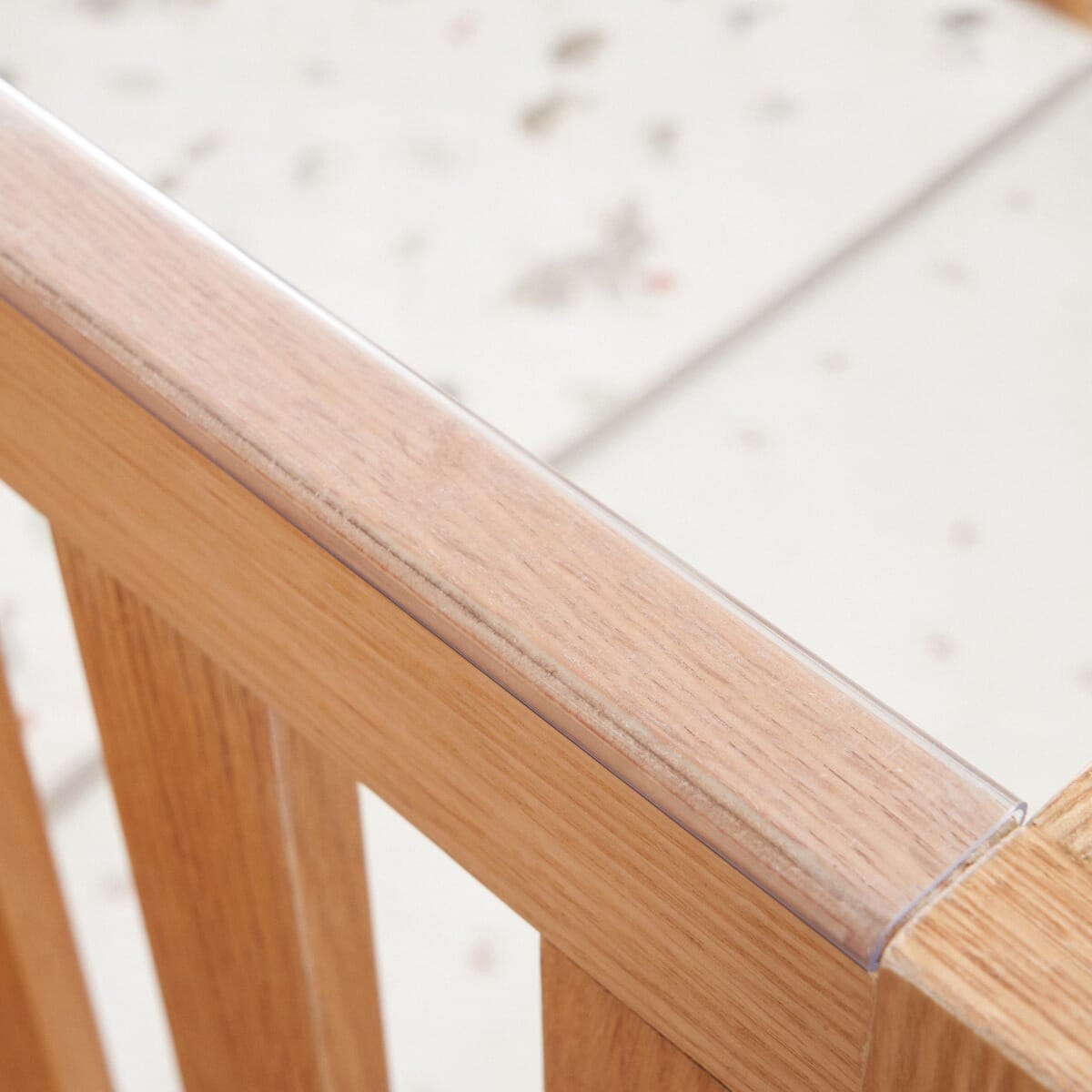 Close-up of the Japandi Mini Cot Bed in light oak showing the clear teething rail. This protective feature helps preserve the natural wood finish while being gentle on baby's gums.