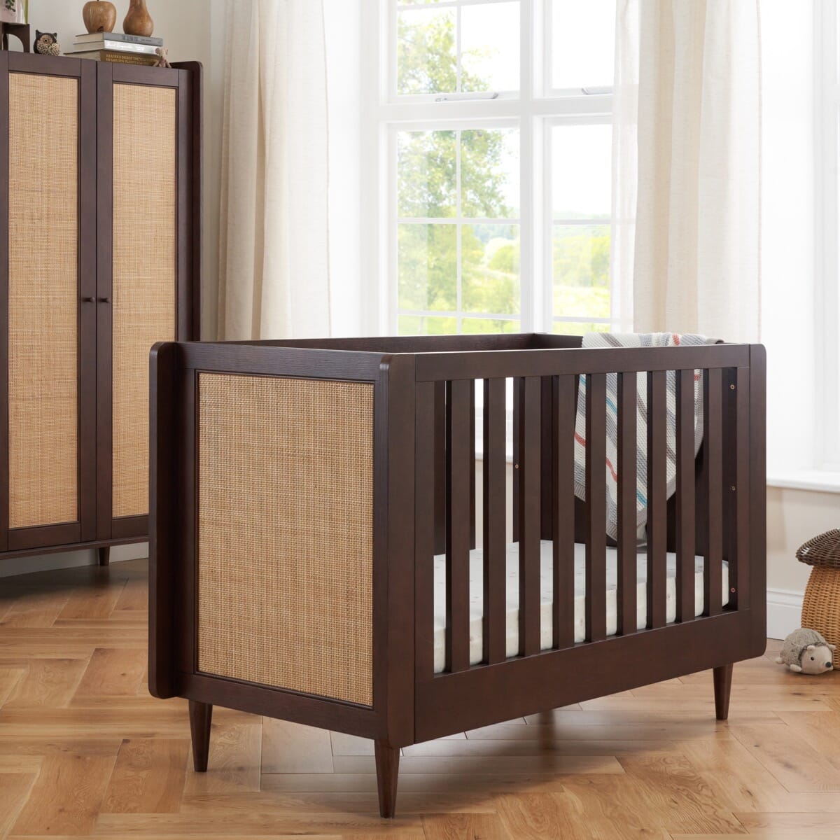 Angled close-up of the japandi mini cot bed in warm walnut with natural rattan panel, highlighting a sturdy build for longevity.