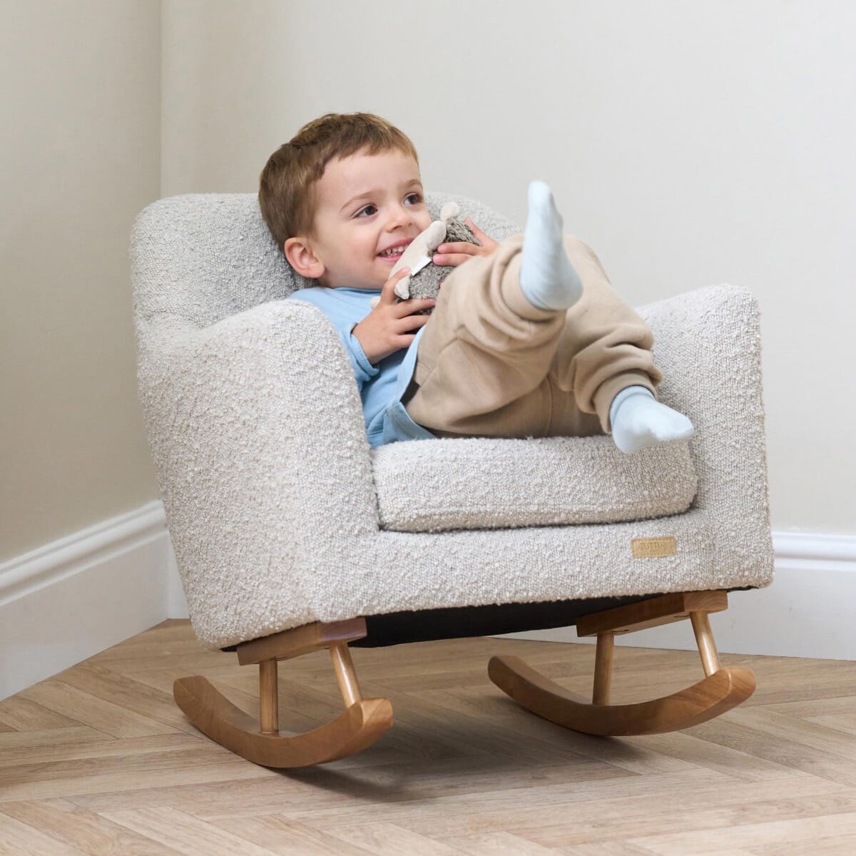 Lifestyle image of a smiling child relaxing in the Jonah Mini Me rocking chair in boucle mushroom, showcasing comfort and scale