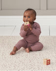 Baby sits on the Bubble Terrazzo play mat holding a wooden block, with soft neutral pattern providing a calm, cushioned play surface