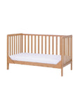 Angled view of the Malmo cot bed in oak finish with open slats and warm tone, showcasing sleek modern lines and timeless appeal