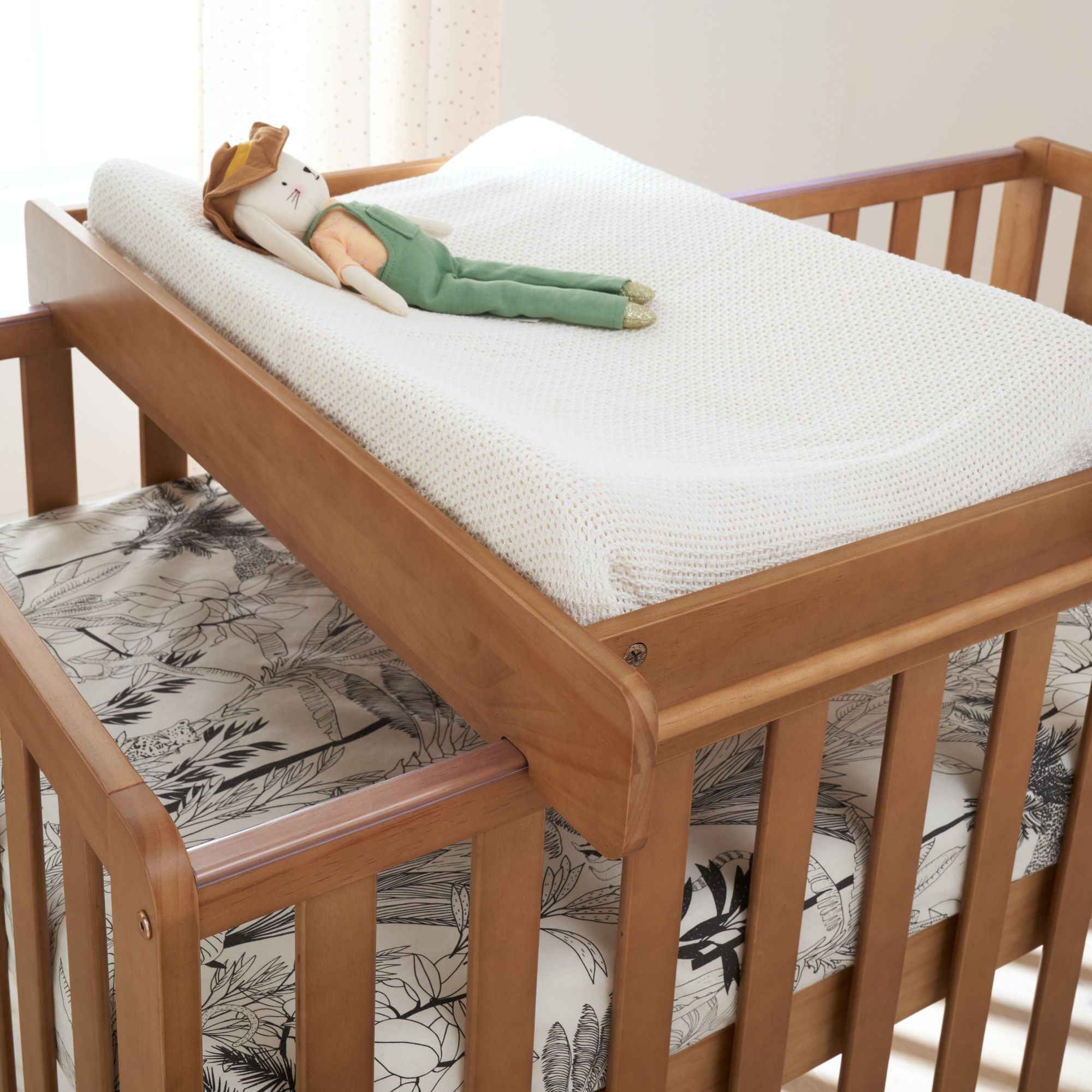 Close-up of Malmo cot bed with cot top changer in oak finish, styled with mattress and toy for added charm