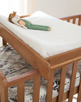 Close-up of Malmo cot bed with cot top changer in oak finish, styled with mattress and toy for added charm