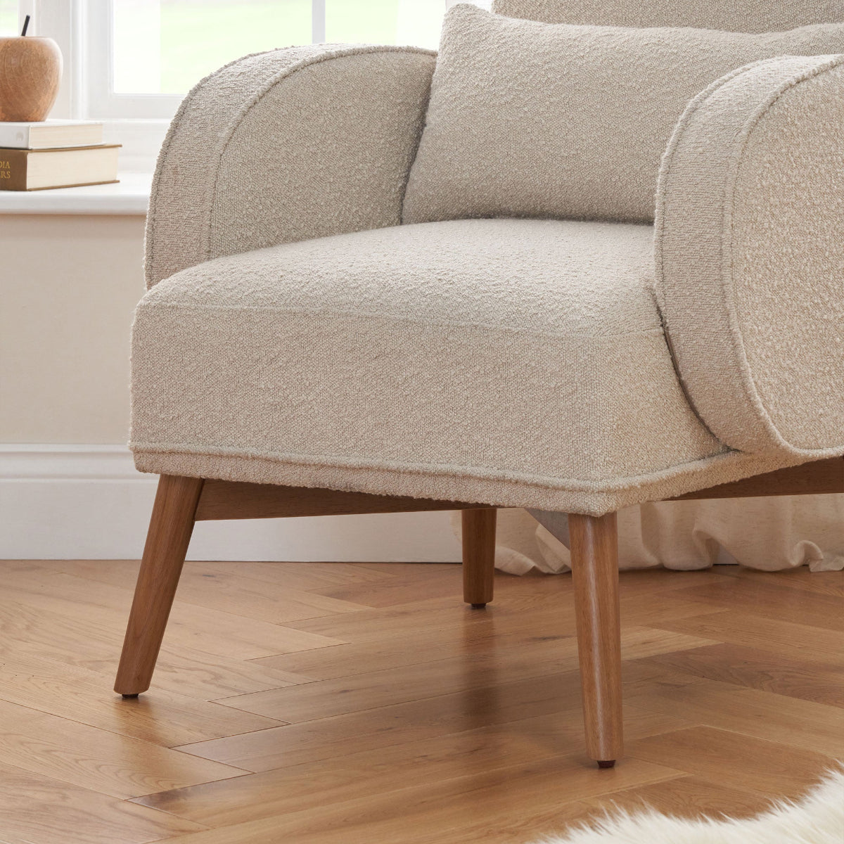 Close-up of the Micah rocking chair in biscuit boucle, showing plush upholstery, lumbar cushion, and wooden legs on parquet flooring.