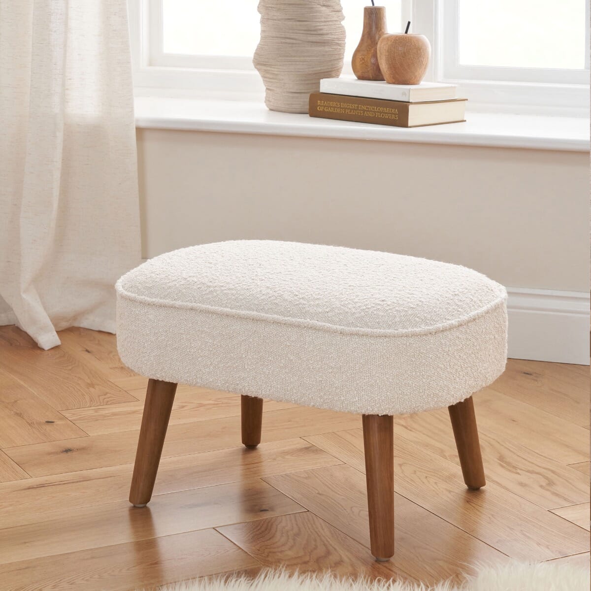 Micah footstool in fresh cream with wooden legs, styled in a cosy room setting with natural wood flooring.