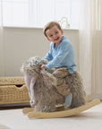 Lifestyle image of a toddler riding Mimi the Mammoth rocking toy, showing supportive handles, gentle rocking motion and playful scale