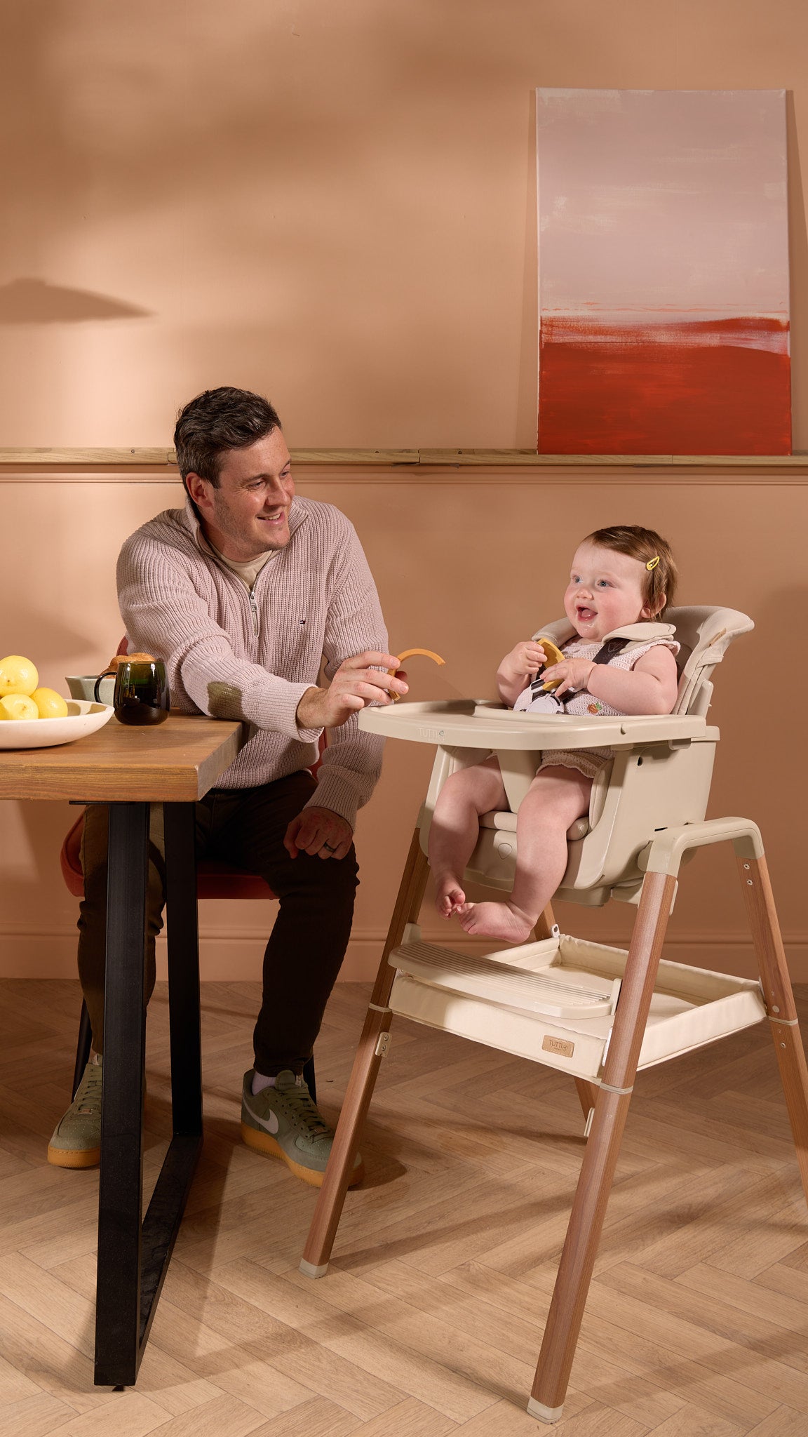 Dad feeding baby seated in the Nova evolutionary highchair – warm family moment with supportive, adjustable tray setup.