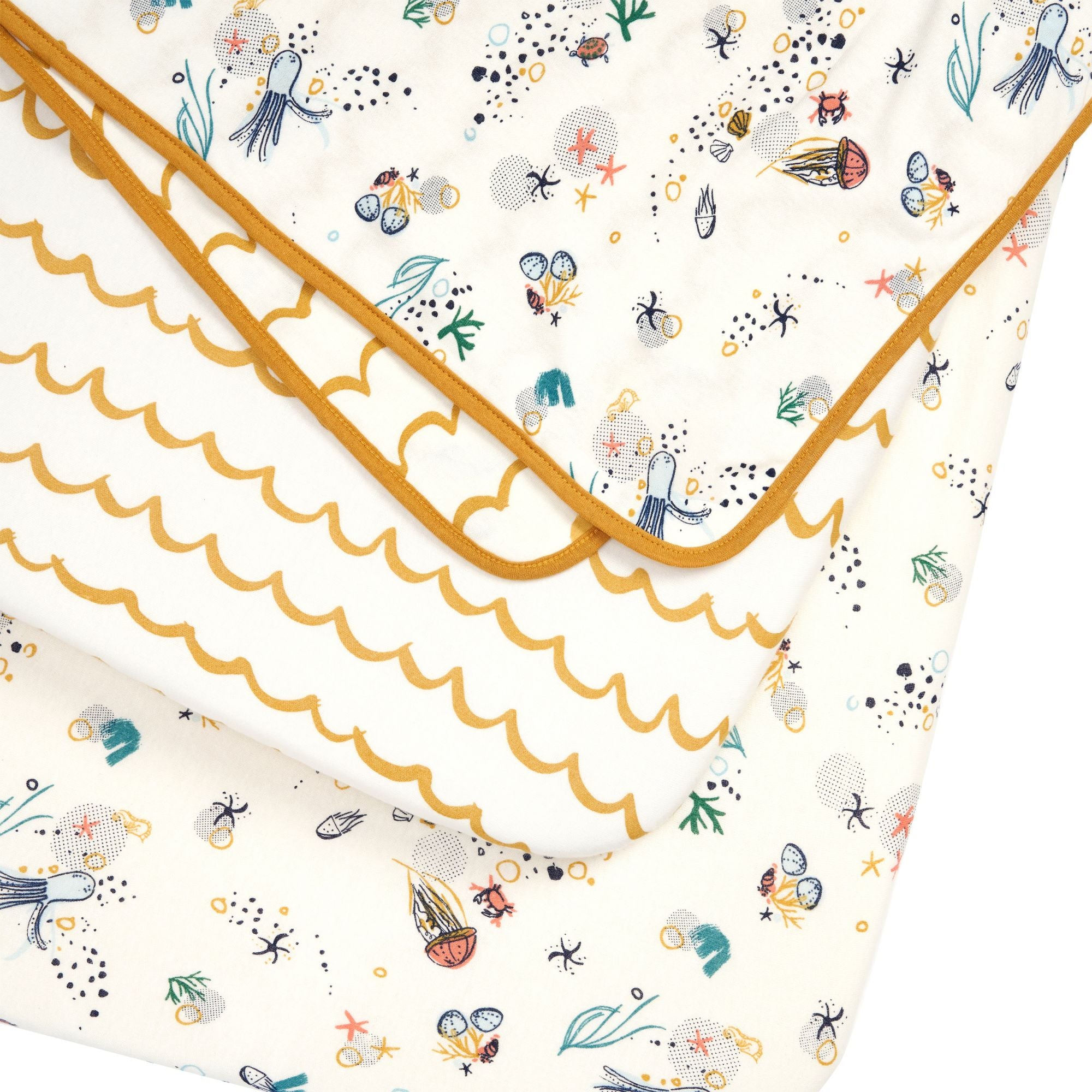 Close-up of Our Planet bedside crib starter pack with fitted sheets and reversible coverlet in soft organic cotton with ocean prints