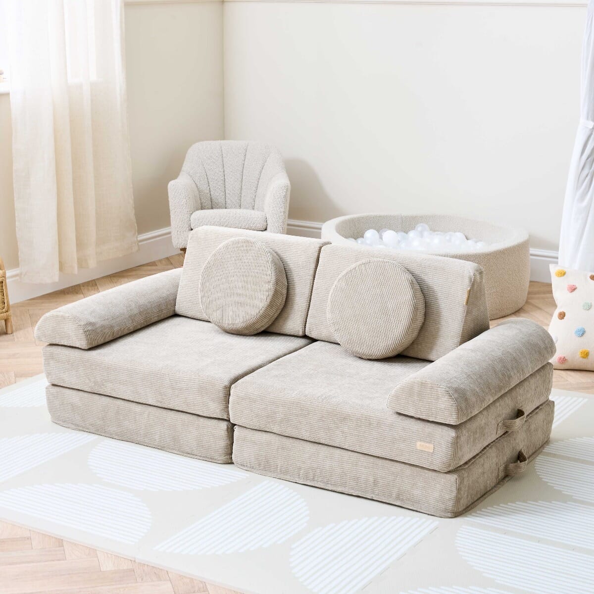 Lifestyle view of the Playrama Montessori Kids Play Sofa in mushroom cord, styled in a nursery with ball pit and armchair for versatile play