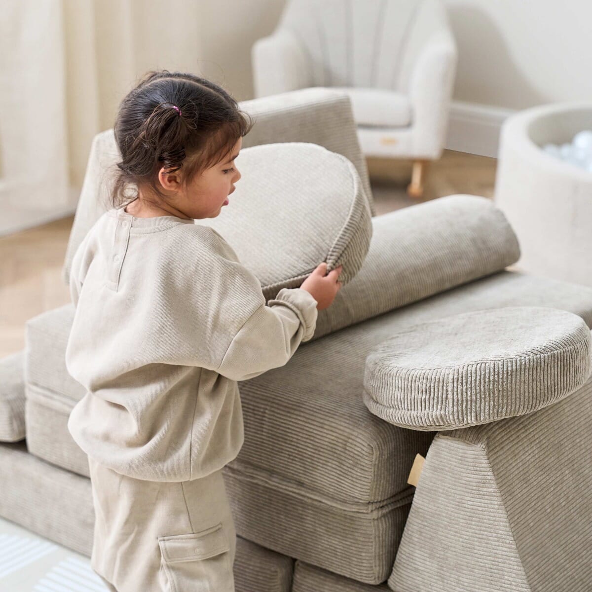 Close-up of toddler holding a round cushion while playing on the Playrama Montessori Kids Play Sofa in mushroom cord, encouraging creativity and fun