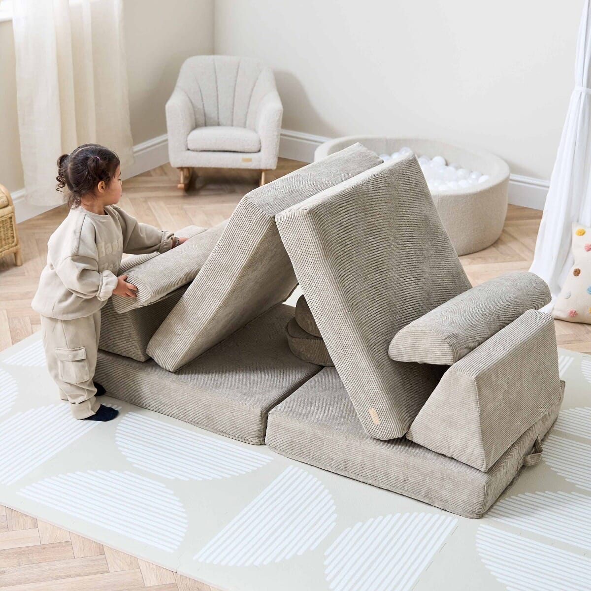Toddler arranging cushions on the Playrama Montessori Kids Play Sofa in mushroom cord finish, styled as a den for imaginative play
