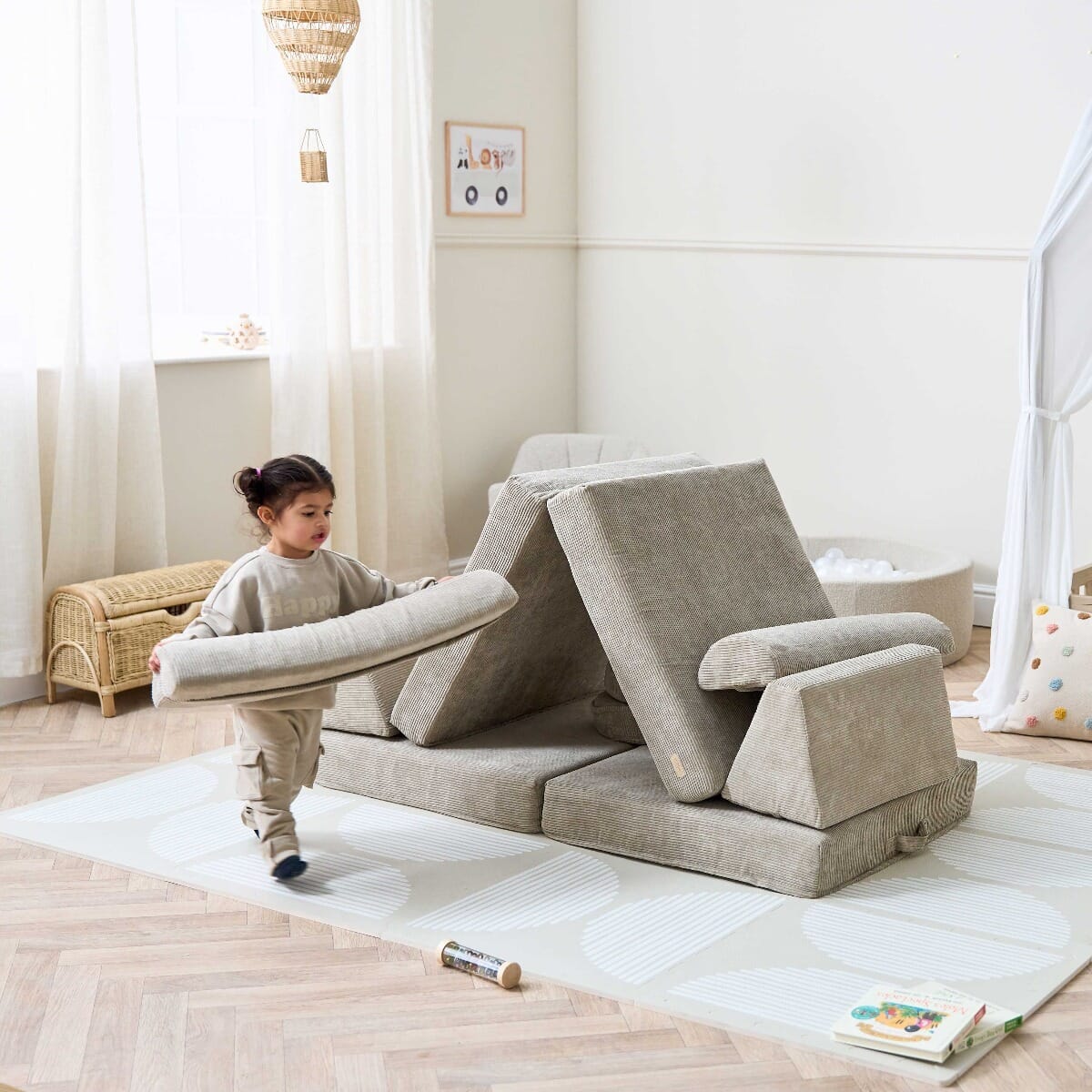 Toddler carrying cushion while playing with the Playrama Montessori Kids Play Sofa in mushroom cord finish, styled as a creative den setup
