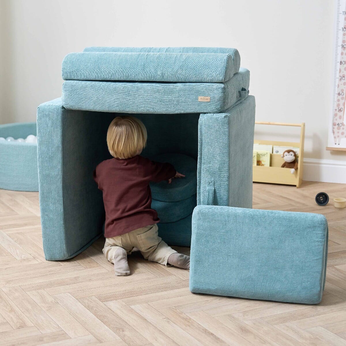 Toddler crawling into a fort built with the Playrama Montessori Kids Play Sofa in ocean stone, showing imaginative play and versatile cushion use