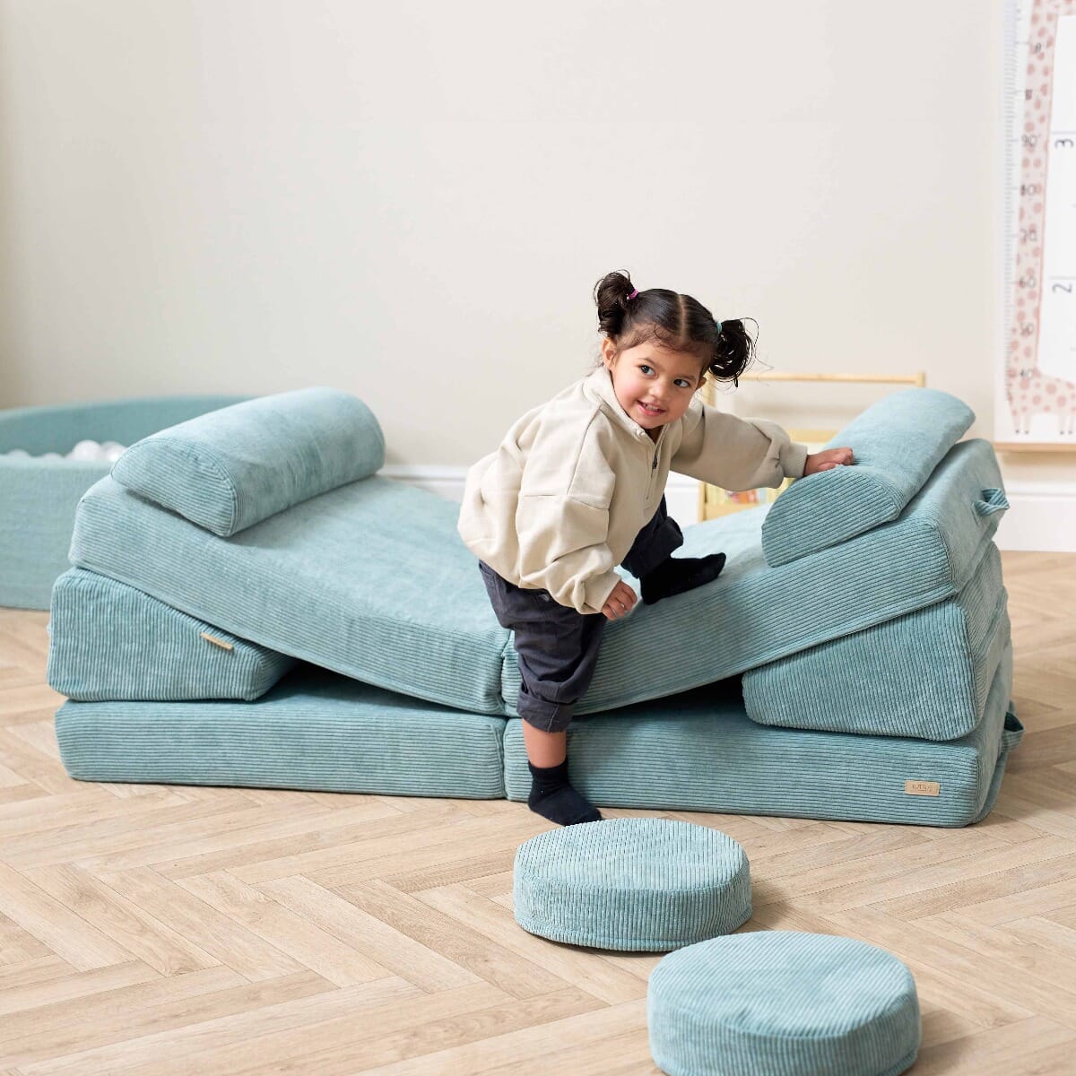 Smiling toddler climbing on the Playrama Montessori Kids Play Sofa in ocean stone, set up as a slope for active play and movement
