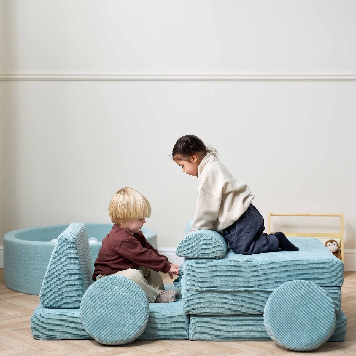 Two toddlers playing together on the Playrama Montessori Kids Play Sofa in ocean stone, styled as a vehicle with circular cushions as wheels
