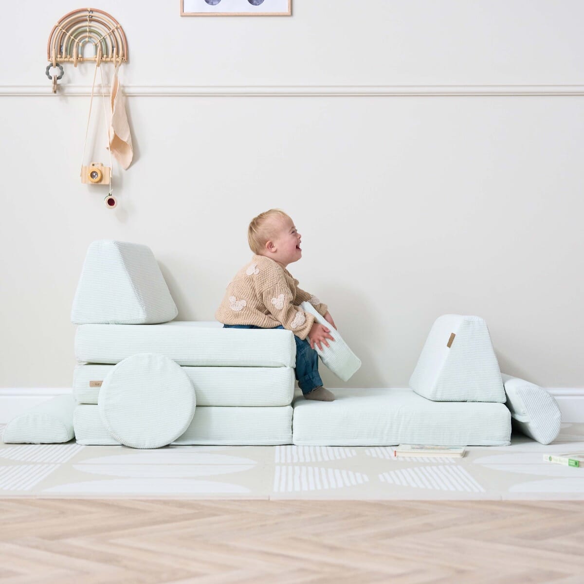Smiling toddler plays on the Playrama Montessori kids play sofa in sea mist, built into a car-shaped setup with cushions and wheels