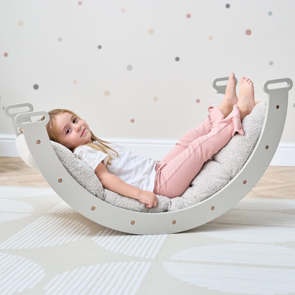 Child relaxing on cushioned arch of the Scala Montessori Pikler frame in mushroom finish, highlighting versatile play and comfort
