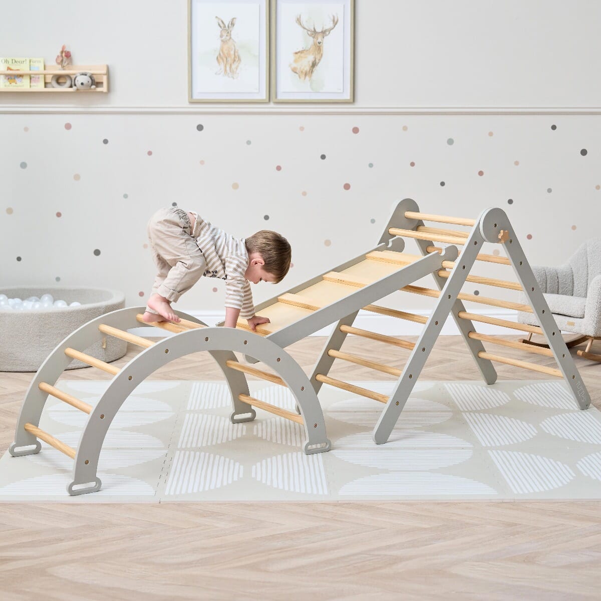 Toddler climbing the Scala Montessori Pikler frame in mushroom finish, building confidence, coordination, and gross motor skills