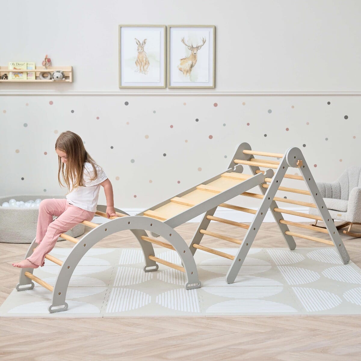 Toddler seated confidently on the Scala Montessori Pikler climbing arch in mushroom finish, exploring balance through playful rest