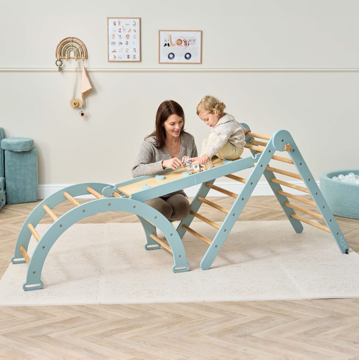 Parent plays with toddler on the Scala Montessori climbing frame in ocean stone, showing the wall and slide attachment for safe, imaginative play