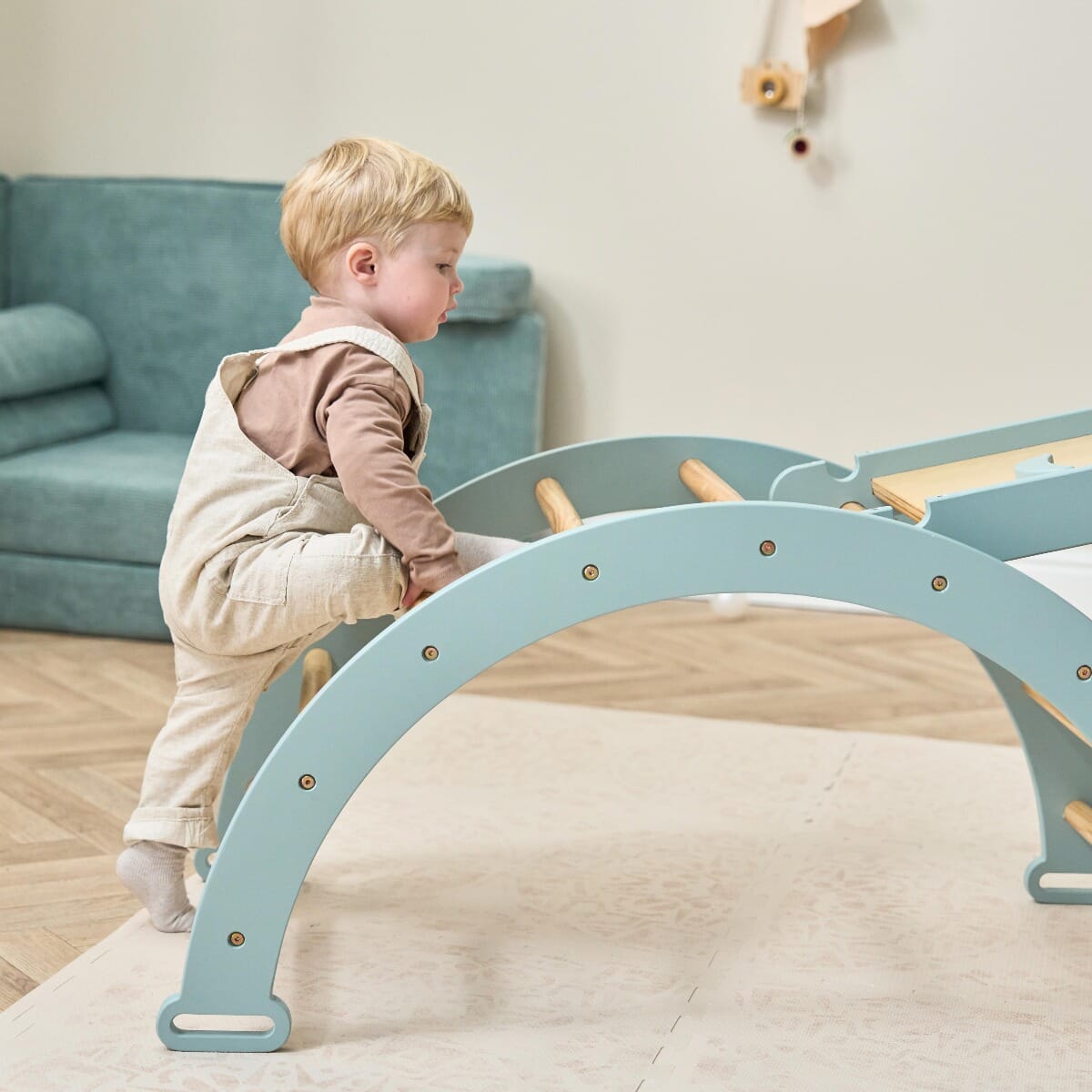 Side view of toddler beginning to climb the Scala Montessori arch in ocean stone, highlighting safe, active play that builds strength and motor skills