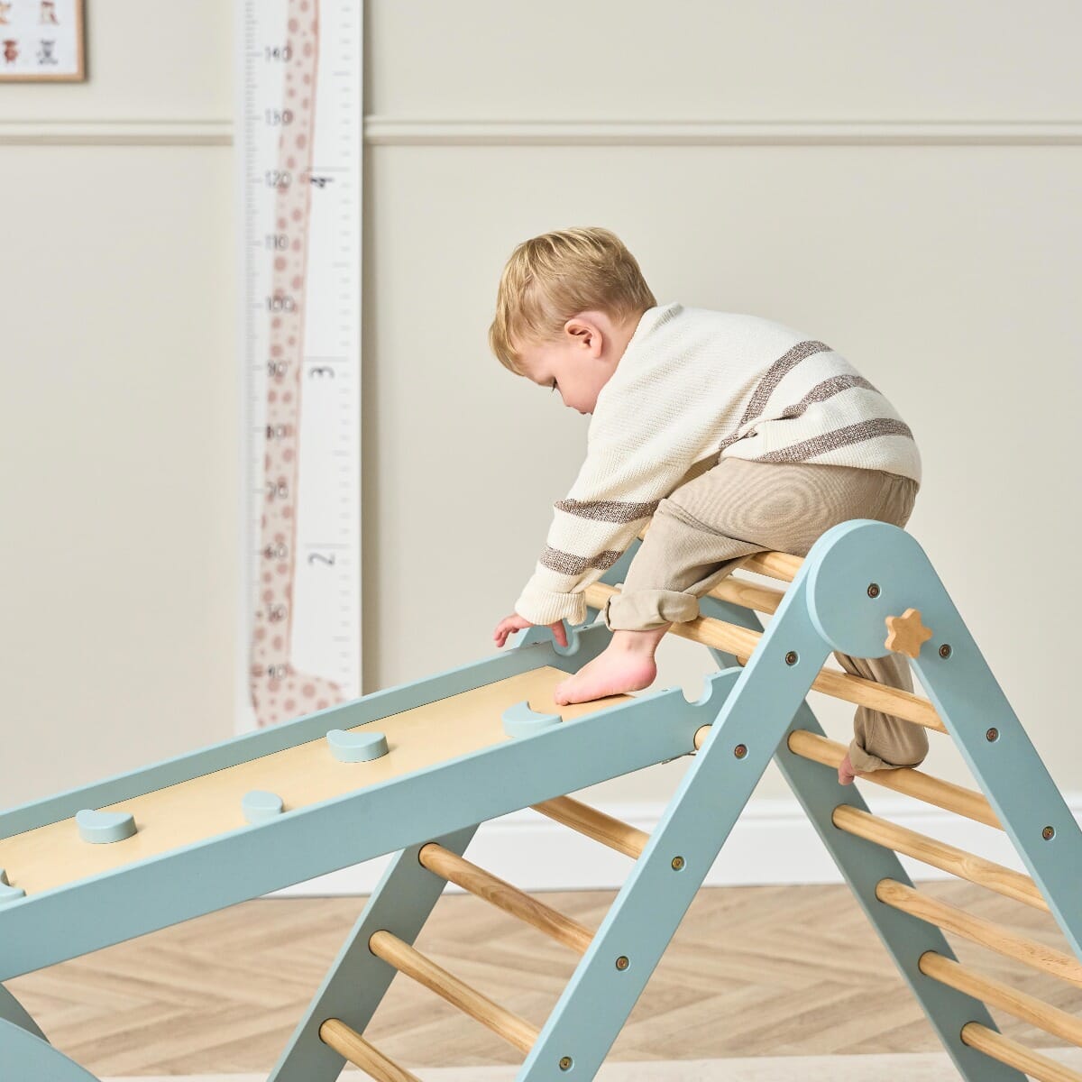 Toddler climbs up the Scala Montessori wall attachment in ocean stone, using wooden grips for balance and coordination, promoting safe independence in play