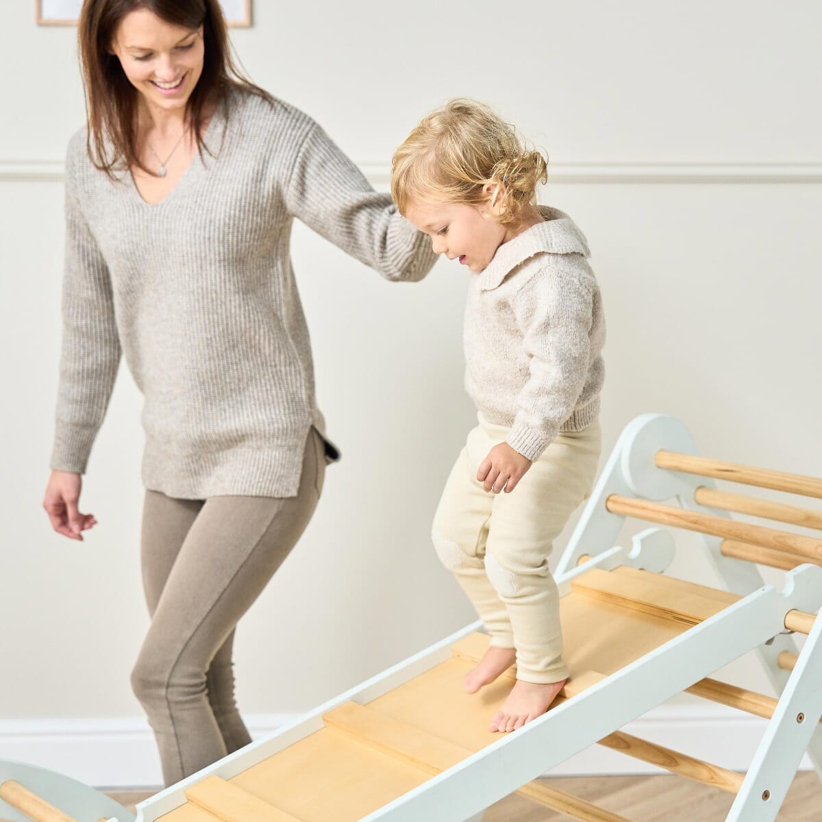 Mum helping toddler explore the Scala Montessori Pikler climbing frame in sea mist, designed for confidence-building and active play