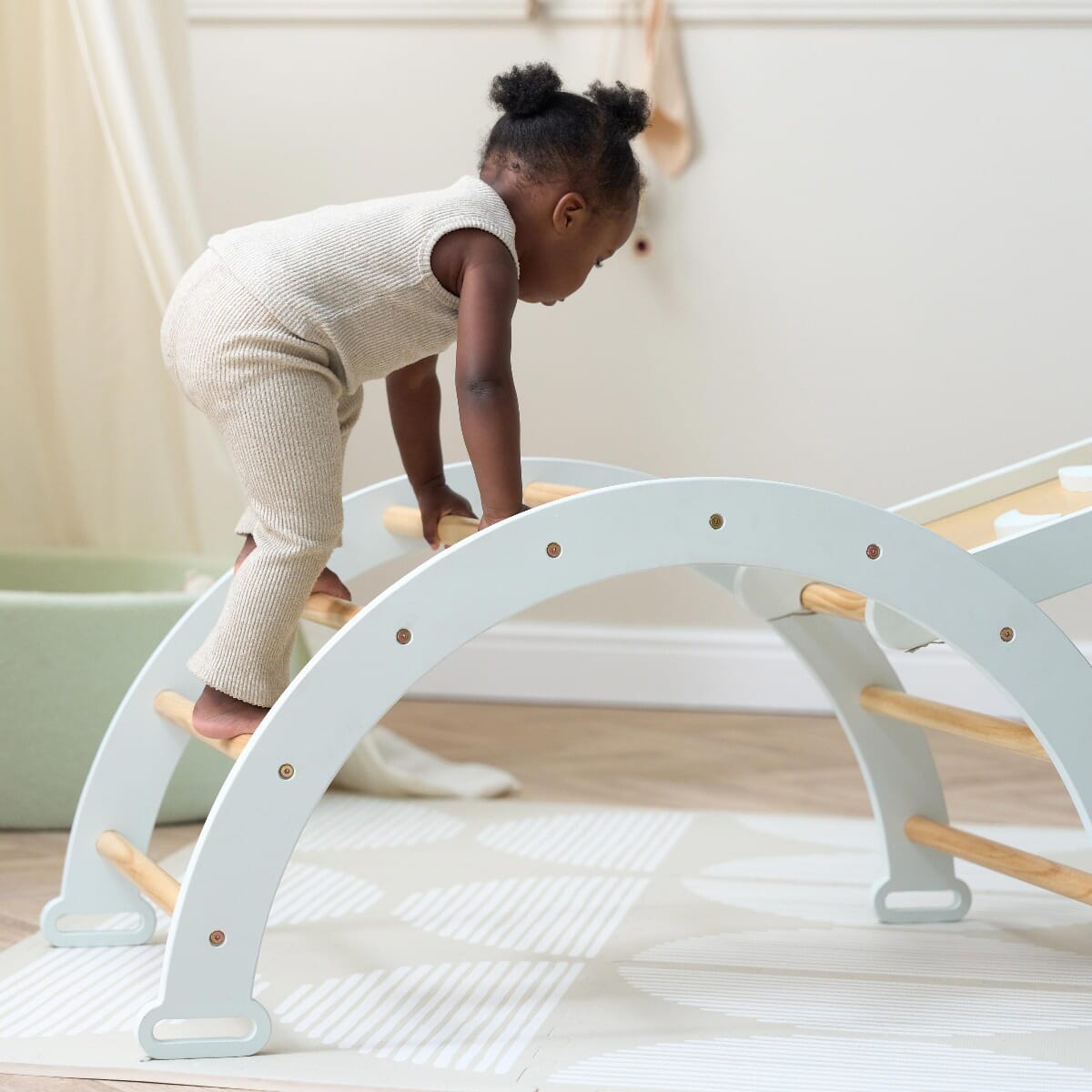 Toddler climbing across the Scala Montessori Pikler arch in sea mist finish, developing balance, strength, and gross motor skills