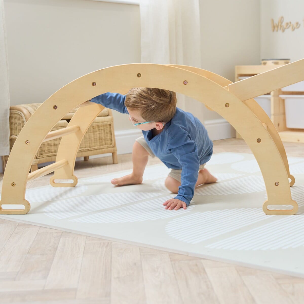 Toddler crawls beneath the Scala Montessori Pikler climbing frame in natural wood, promoting gross motor skills and imaginative exploration